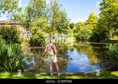Donna in piedi presso lo stagno del villaggio con anatre su di esso Nel villaggio di Chiltern Hills di Ewelme Oxfordshire Inghilterra Foto Stock