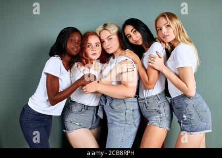 Ritratto di cinque belle donne in jeans in piedi insieme isolati su sfondo grigio Foto Stock