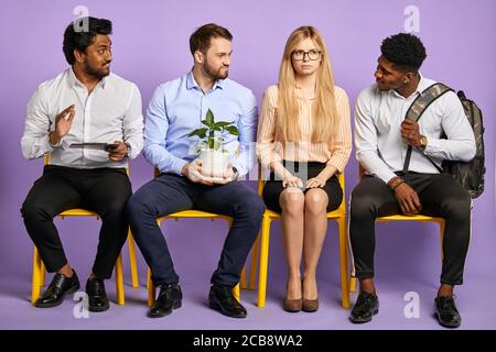 uomini multietnici che flirtare con una giovane bella donna bionda in occhiali in attesa di un colloquio di lavoro Foto Stock