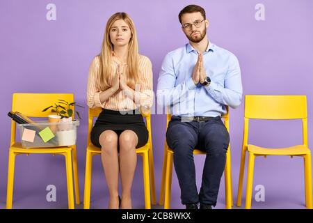 triste giovane donna e uomo che chiede perdono e uno più possibilità di tenere le mani pleading guardando in macchina fotografica e in attesa per un colloquio di lavoro Foto Stock