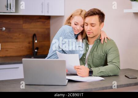 coppia che legge documenti legali a casa utilizzando un computer portatile moderno, la famiglia che considera un mutuo o un'assicurazione, lo studio dei dettagli del contratto, discutere la conditio Foto Stock