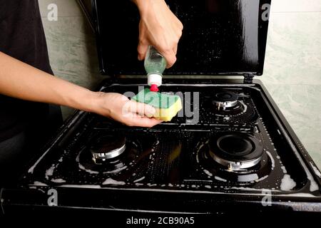 Pulire la stufa a gas in cucina con detergente e una spugna. Elettrodomestici per la cottura. Pulizia delle superfici. Foto Stock