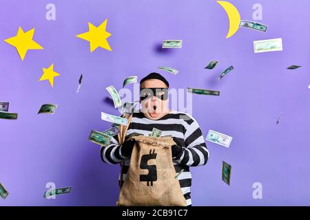 un uomo eccitato che tiene un moneybag e sorpreso di volare soldi di carta. primo piano ritratto. isolato sfondo blu. studio scatto Foto Stock