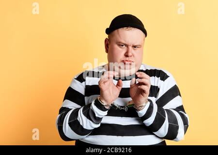 accigliato triste infelice uomo grasso in vestiti a strisce guardando la macchina fotografica. isolato sfondo giallo. Foto Stock