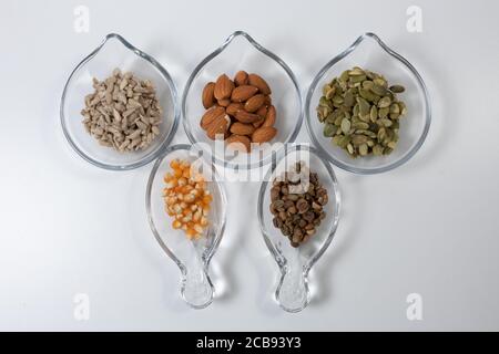 Semi vari - girasole, mandorle, semi di zucca, mais e caffè in coppe di vetro diferenti su sfondo bianco. Foto Stock