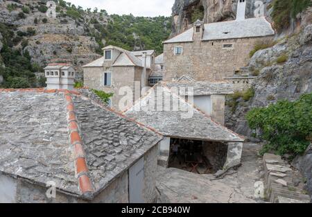 All'esterno case e area dell'antico monastero nella parte laterale della montagna. Case bianche e grigie nel deserto di Blaca sull'isola di Brac Foto Stock