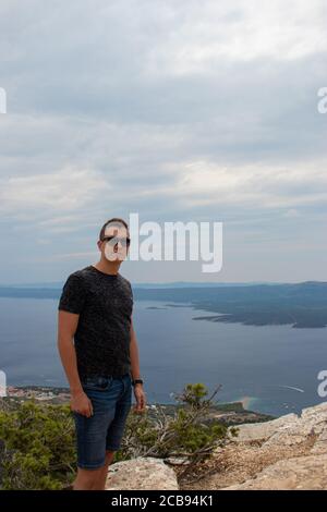 Scatto verticale di un giovane adulto che si pone sulla cima del monte Vidova gora, punto più alto dell'isola di Brac. Luogo popolare per i turisti a prendere il ph Foto Stock