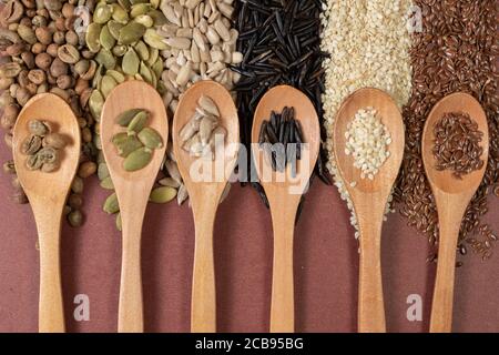 Semi diversi in cucchiai di legno su una superficie di diverso semi e sfondo marrone Foto Stock