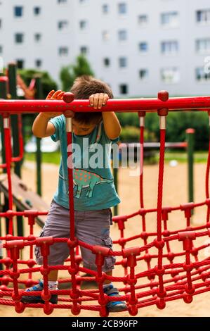 POZNAN, POLONIA - 26 luglio 2020: Giovane polacco di tre anni caucasico ragazzo in piedi su un ponte rosso rete di un equipaggiamento in un parco giochi. Foto Stock