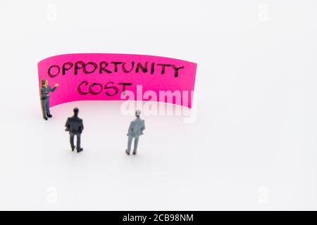 Incontro di presentazione con figurine in miniatura poste come uomini d'affari in piedi Davanti alla nota post-it con messaggio scritto a mano sul costo dell'opportunità poll Foto Stock