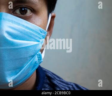 Colpo di testa di un uomo indiano che indossa una maschera chirurgica al naso guardando la fotocamera per la protezione da virus corona o covid-19 Foto Stock