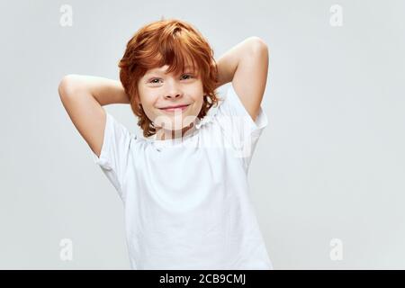 Il ragazzo dai capelli rossi tiene le mani dietro la sua testa sorridi t-shirt bianca studio Foto Stock