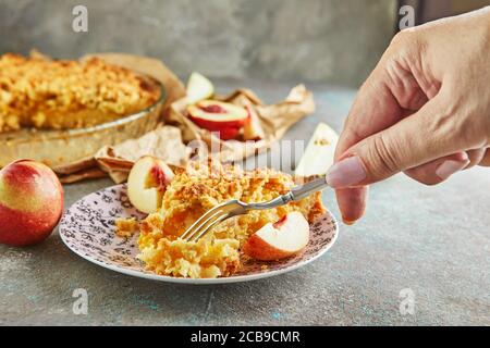 La mano della donna con una forchetta, rompe un pezzo di torta con pesche e pere, torte fatte in casa. Foto Stock