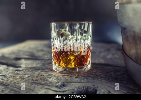 Bicchiere con brandy al rum di whisky o bourbon su un vecchio tavolo vicino a un barile di legno Foto Stock