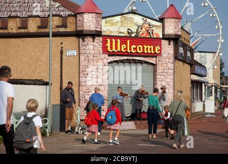 Portobello, Edimburgo, Scozia, Regno Unito. 12 agosto 2020. Gli studenti della scuola primaria di Towerbank si fanno strada alle lezioni con un salto nel loro passo, mentre sono intrattenuti dalle Signore della band Fun Fiddlers in bel sole. I bambini tornano a scuola per la prima volta in più di quattro mesi a causa della pandemia del Covid-19, seguita dalle vacanze estive della scuola scozzese. Foto Stock