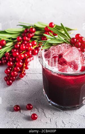 Cocktail di frutta fresca ghiacciata in vetro, rinfrescante bevanda estiva al ribes rosso con foglia di rosmarino su fondo di pietra in cemento, vista angolare Foto Stock