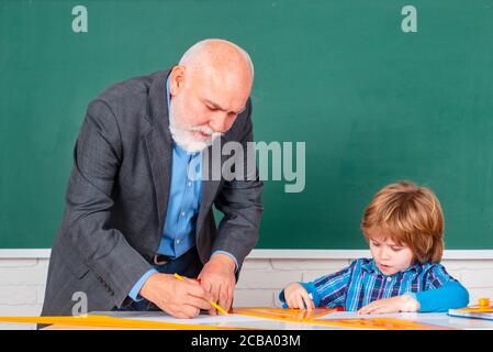 Alunno in classe pareggio con insegnante. Scuola elementare insegnante di nonno che dà sostegno alla pupilla femminile in classe. Processo educativo. Foto Stock