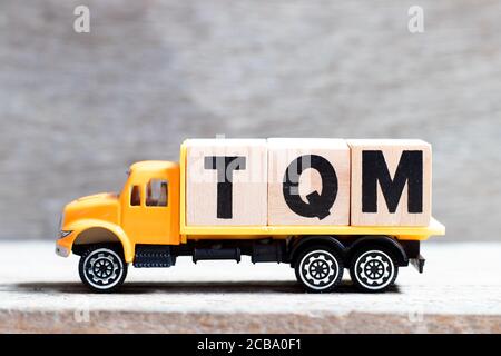 Blocco di lettere di mantenimento carrello nella parola TQM (Abbreviazione della gestione della qualità totale) su sfondo di legno Foto Stock