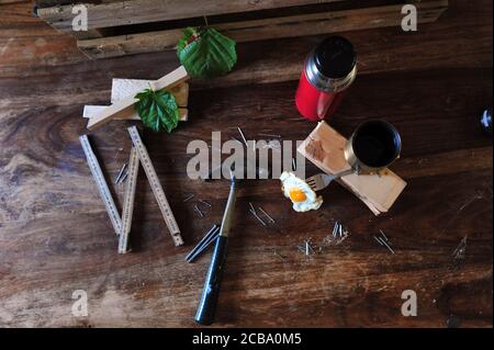 Vista ad alto angolo di attrezzi da falegname, thermos e uovo fritto sulla forchetta. Immagine orizzontale. Foto Stock