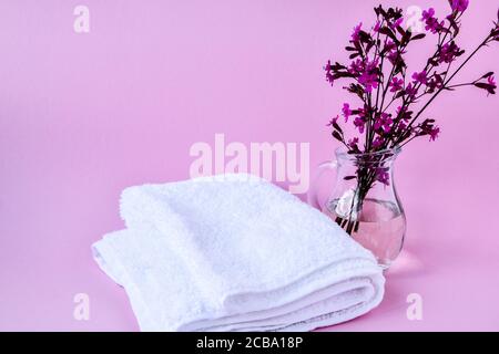 Asciugamani di cotone bianco puliti e freschi, trattamento Spa con ramo fiorito su sfondo rosa Foto Stock