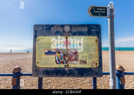 Un cartello del Sentiero dell'eredità dell'Hythe intemperie sulla Marine Parade lungo l'England Coast Path, Inghilterra Foto Stock