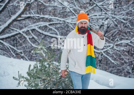 Divertente Santa uomo in posa con l'ascia e l'albero di Natale. Uomo lumberman con albero di Natale nel parco invernale. Felice padre con albero di Natale su una neve Foto Stock