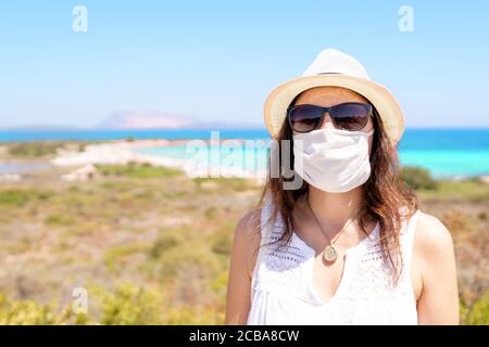 Giovane caucasica che posa per un quadro con protezione di Coronavirus maschera in vacanza estiva con mare tropicale luminoso e colorato sullo sfondo Foto Stock