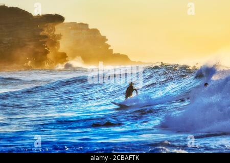 Un gruppo di surfisti che galleggiano e cavalcano un'onda alla spiaggia di Bronte, nella periferia orientale di Sydney, costa del Pacifico all'alba. Foto Stock