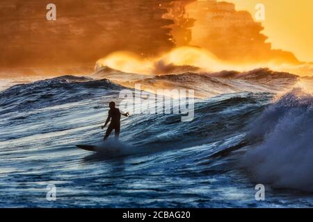 Surfer maschile singolo irriconoscibile scivola l'onda alla spiaggia di Bronte di Sydney Eastern Suburbs sulla costa dell'oceano Pacifico in sole mattine. Foto Stock