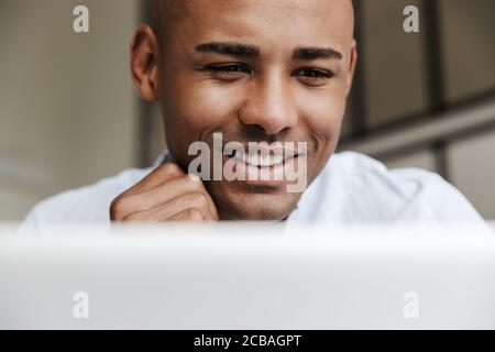 Foto closeup di gioioso afroamericano che lavora con il computer portatile e sorridendo in salotto Foto Stock