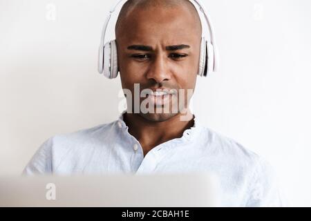 Foto closeup di un uomo afro-americano calvo che lavora con le cuffie con un computer portatile a casa Foto Stock