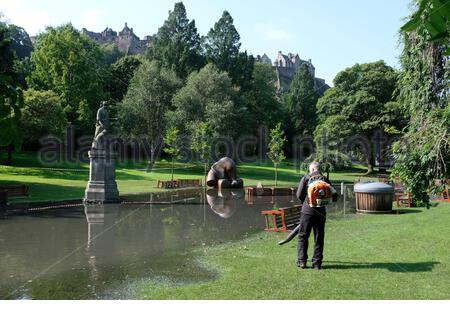 Edimburgo, Scozia, Regno Unito. 12 agosto 2020. Il tempo soleggiato sostituisce le tempeste notturne che lasciano i West Princes Street Gardens allagati e cordonati al pubblico. Scultura in bronzo elefante intrappolata nelle acque alluvionali. Vista sul Castello di Edimburgo. Credit: Craig Brown/Alamy Live News Foto Stock