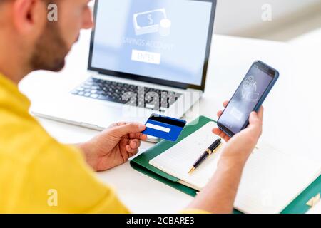 Vista posteriore di un uomo che tiene la sua carta di credito in mano mentre fa online banking sul telefono cellulare. Foto Stock