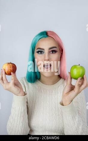 giovani donne con capelli tinti nei colori blu e rosa e tenendo mele verdi e rosse Foto Stock