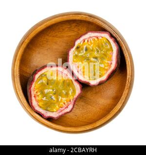 Frutta fresca di passione tagliata in due metà, in ciotola di legno. Frutti con pelle viola e polpa gialla con molti semi. Può essere mangiato crudo. Foto Stock