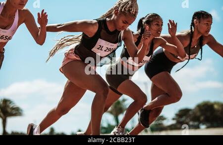 Atleti che iniziano per una gara su una pista da corsa. Corridore femminile che inizia uno sprint al circuito dello stadio. Foto Stock