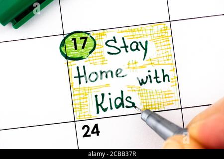 Le dita della donna con la penna che ricorda di scrivere rimangono a casa con i bambini in calendario. Agosto 17. Foto Stock