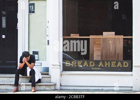 Un uomo si siede stanco fuori da un negozio che è chiuso in Hampstead High Street come affari vicino tutto il Regno Unito a causa del Coronavirus o Covid-19. Foto Stock