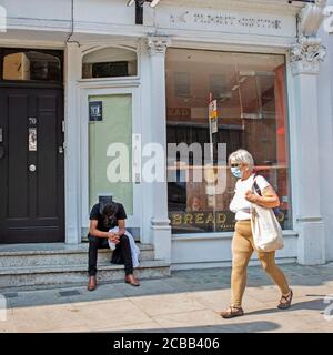 Un uomo si siede stanco fuori da un negozio che è chiuso in Hampstead High Street come affari vicino tutto il Regno Unito a causa del Coronavirus o Covid-19. Foto Stock