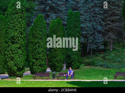 Uomo sovrappeso in un canotta e pantaloni si siede su un parco bench.Unhealthy lifestyle. Tatuaggi sul braccio. Weight loss.Kislovodsk, Russia, 4 agosto 2020 Foto Stock