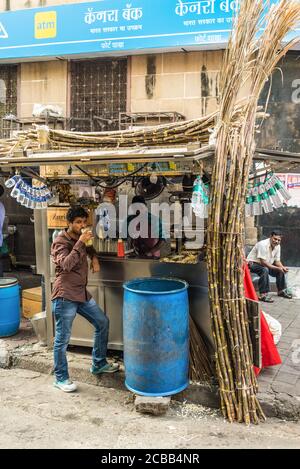 Mumbai, India - 22 novembre 2019: L'uomo locale inideale beve succo di canna da zucchero sulla strada a Mumbai, India. Mumbai è famosa per il suo cibo di strada. Foto Stock