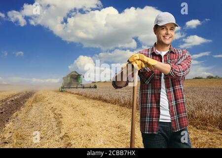 Agricoltore maschio in piedi su un campo di grano con una mietitrebbia trebbiatrice nella parte posteriore Foto Stock