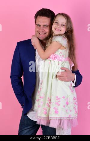 Ragazza e uomo con facce sorridenti felici su sfondo rosa. Figlia e papà si abbracciano. Concetto di infanzia e famiglia. Studentessa si trova accanto al padre Foto Stock