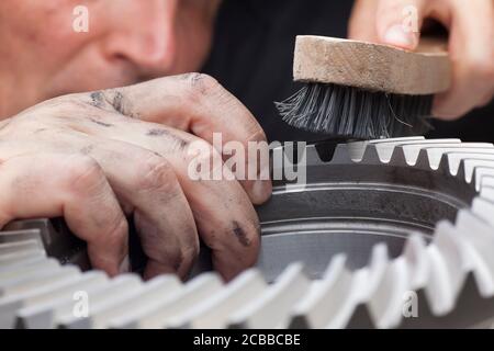 Meccanico con mani sporche pulendo una ruota dentata con un spazzola in acciaio - fuoco selettivo sulla mano Foto Stock