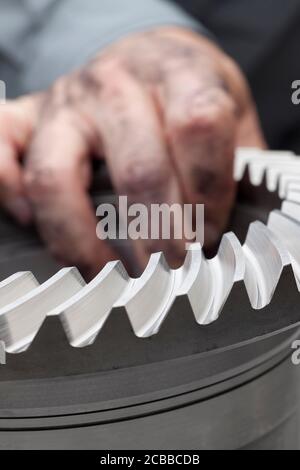 Mano sporca di un meccanico che tiene una ruota dentata grande - fuoco selettivo in primo piano Foto Stock
