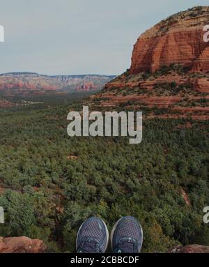 Le punte delle scarpe di un escursionista seduto su una sporgenza che domina le valli piene di alberi e le montagne di Sedona, Arizona, Stati Uniti Foto Stock