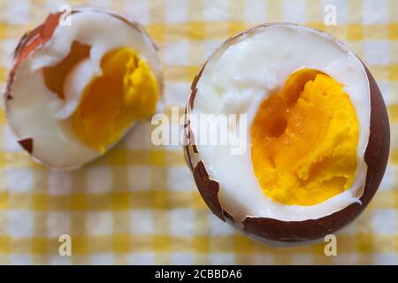 M&S British Farmed Free Range Maran Island Brown Egg on serviette di tovagliolo giallo e bianco - uovo bollito con taglio superiore per mostrare il tuorlo Foto Stock