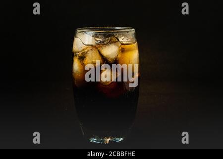 Un bicchiere fresco di bevanda a base di cola con ghiaccio, bolle e frizzante. Cola in vetro con cubetti di ghiaccio isolati su sfondo scuro. Concetto di bevande e prodotti. Foto Stock