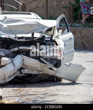 Primo piano di un'auto bianca distrutta durante un incidente d'auto. Paraurti anteriore, motore, fari danneggiati. Le lesioni non sono compatibili con la vita Foto Stock
