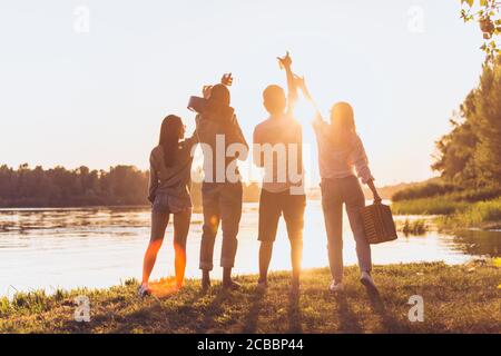 Gruppo di amici che camminano giù durante il picnic alla spiaggia sotto la luce del tramonto del sole. Stile di vita, amicizia, divertimento, weekend e riposo concetto. Sembra allegro, felice, festoso, festoso. Foto Stock